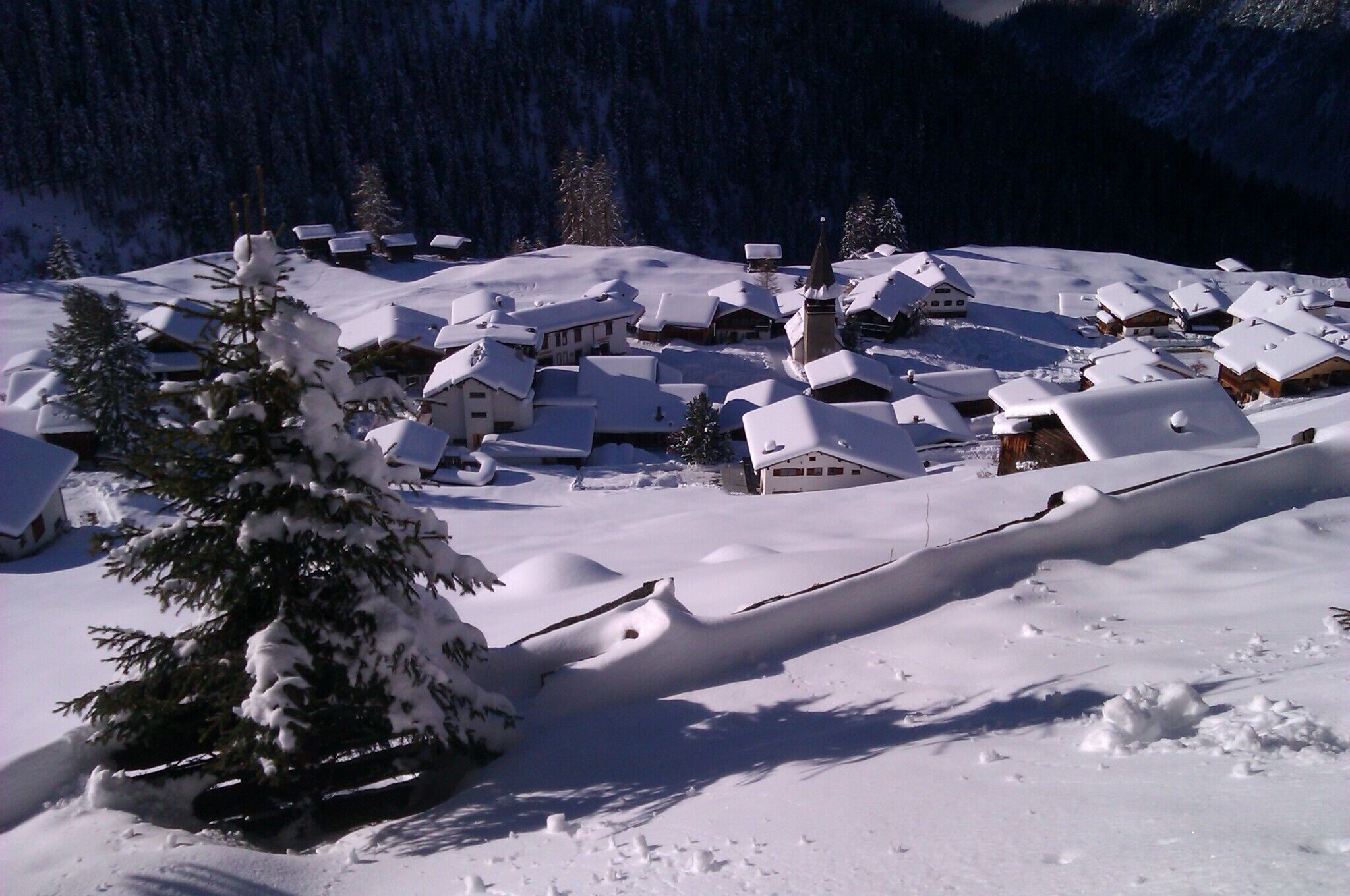 A snow-covered village with traditional houses and a church, surrounded by mountains.
