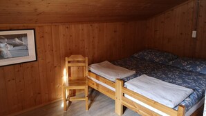 A wooden cabin room with a bunk bed, a wooden chair, and a framed picture on the wall.