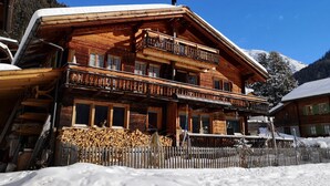 A wooden chalet with a balcony, a covered porch, and a snow-covered roof.