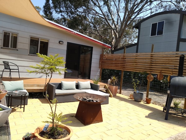 Relax in a serene outdoor space with a wicker sofa, small table, and chairs, surrounded by lush greenery and a barbecue grill.