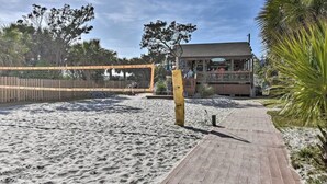 Ein Beachvolleyballfeld mit Holzzaun, einer Holzpromenade und einem Gebäude mit Balkon im Hintergrund.
