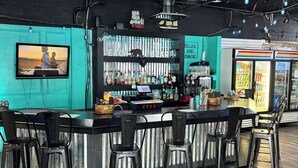 Eine Bar mit einem türkisfarbenen Akzentwand, einem großen Fernsehbildschirm und einer Theke mit Hockstühlen.