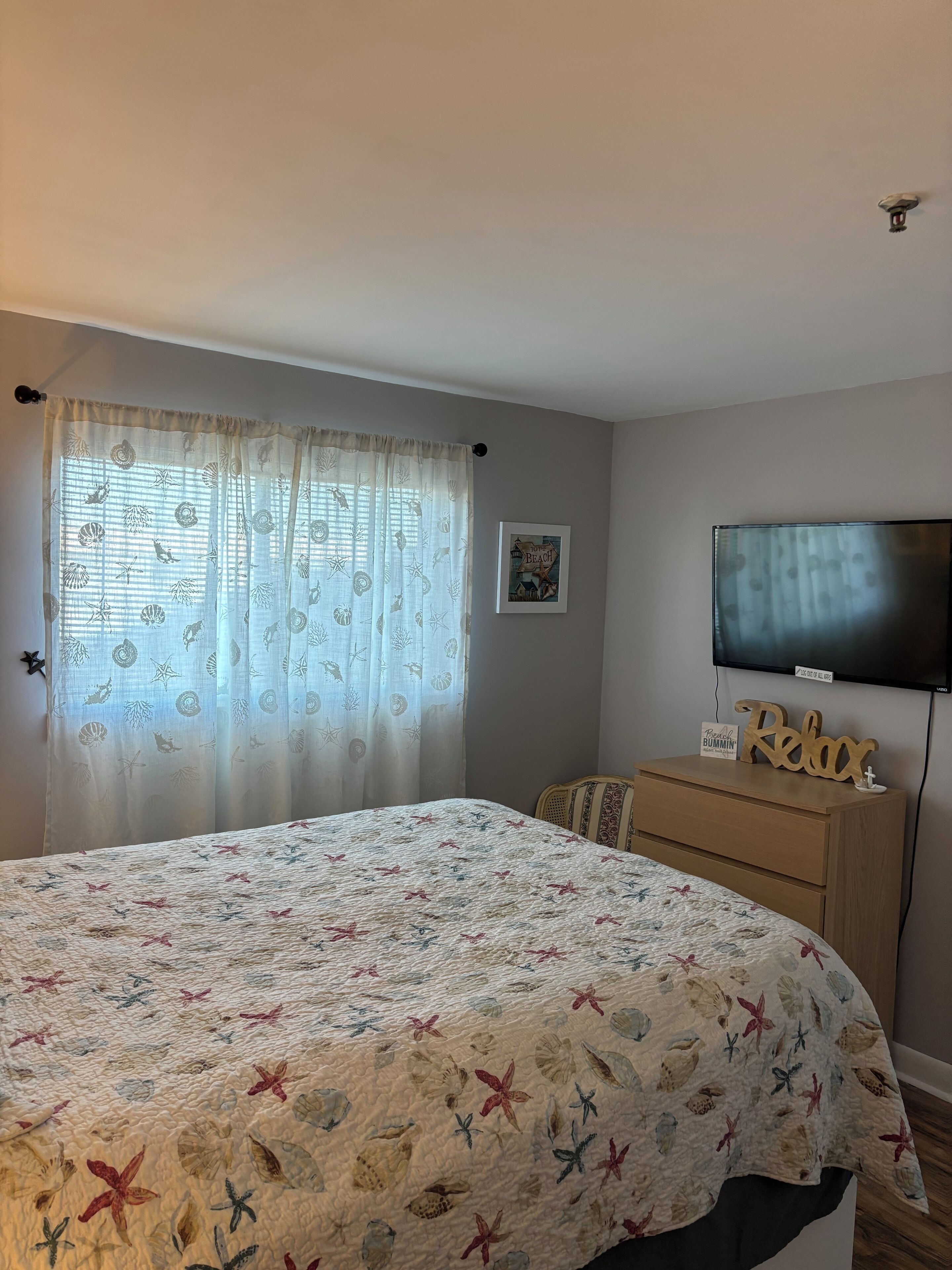 A bedroom with a bed, a dresser, a television, and a window with curtains.