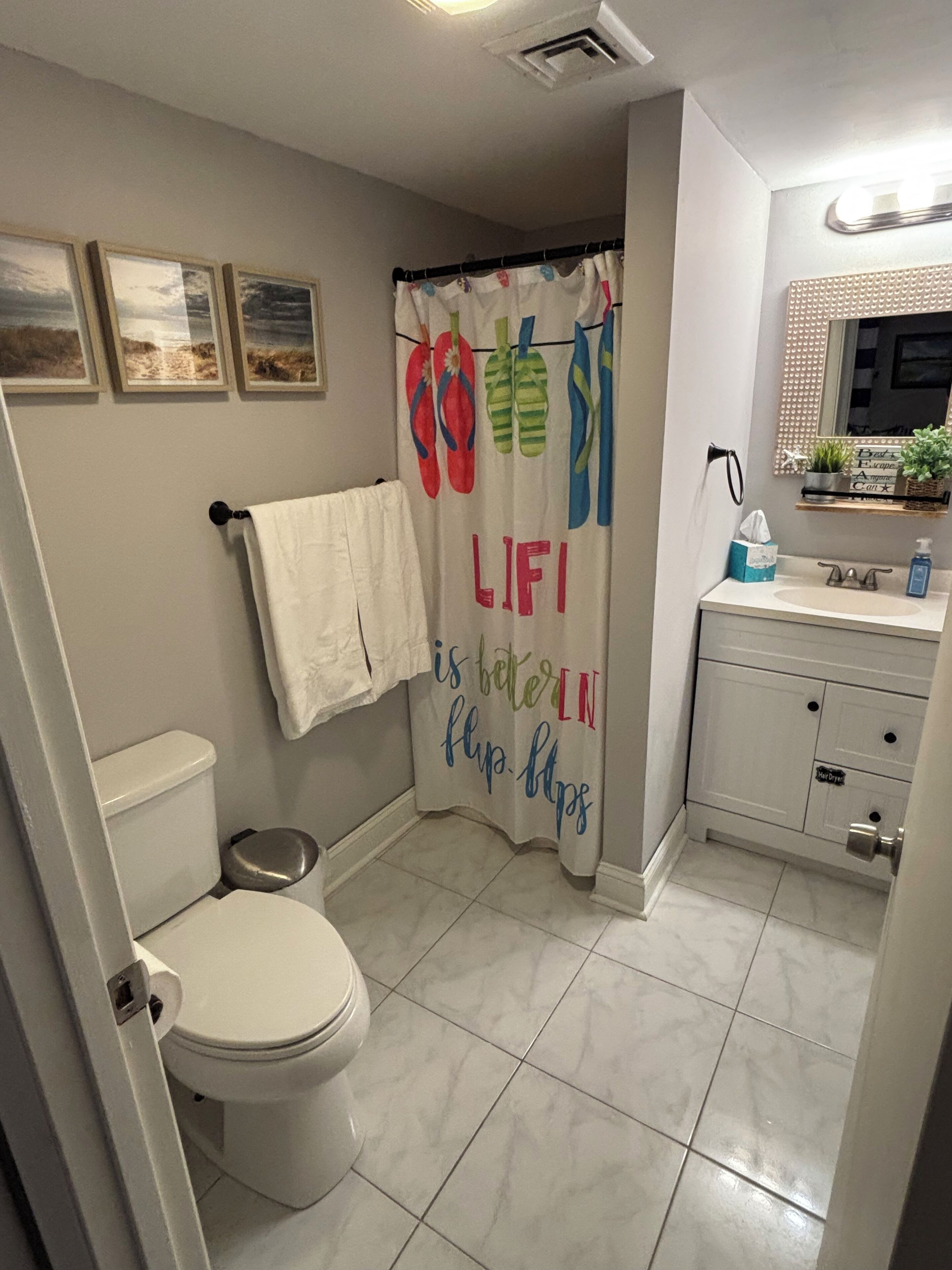 Een badkamer met toilet, douchegordijn met flip-flop motieven, wastafel en spiegel.