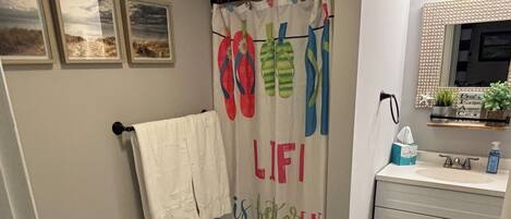 Een badkamer met toilet, douchegordijn met flip-flop motieven, wastafel en spiegel.