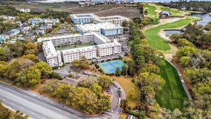 Eine Vogelperspektive auf einen Hotelkomplex mit mehreren Gebäuden, einem Golfplatz und einem Gewässer im Hintergrund.