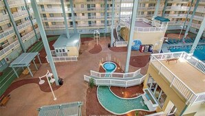 Ein mehrstöckiges Hotel mit Innenhof, der einen Swimmingpool, Sitzgelegenheiten im Freien und einen Spielbereich für Kinder bietet.
