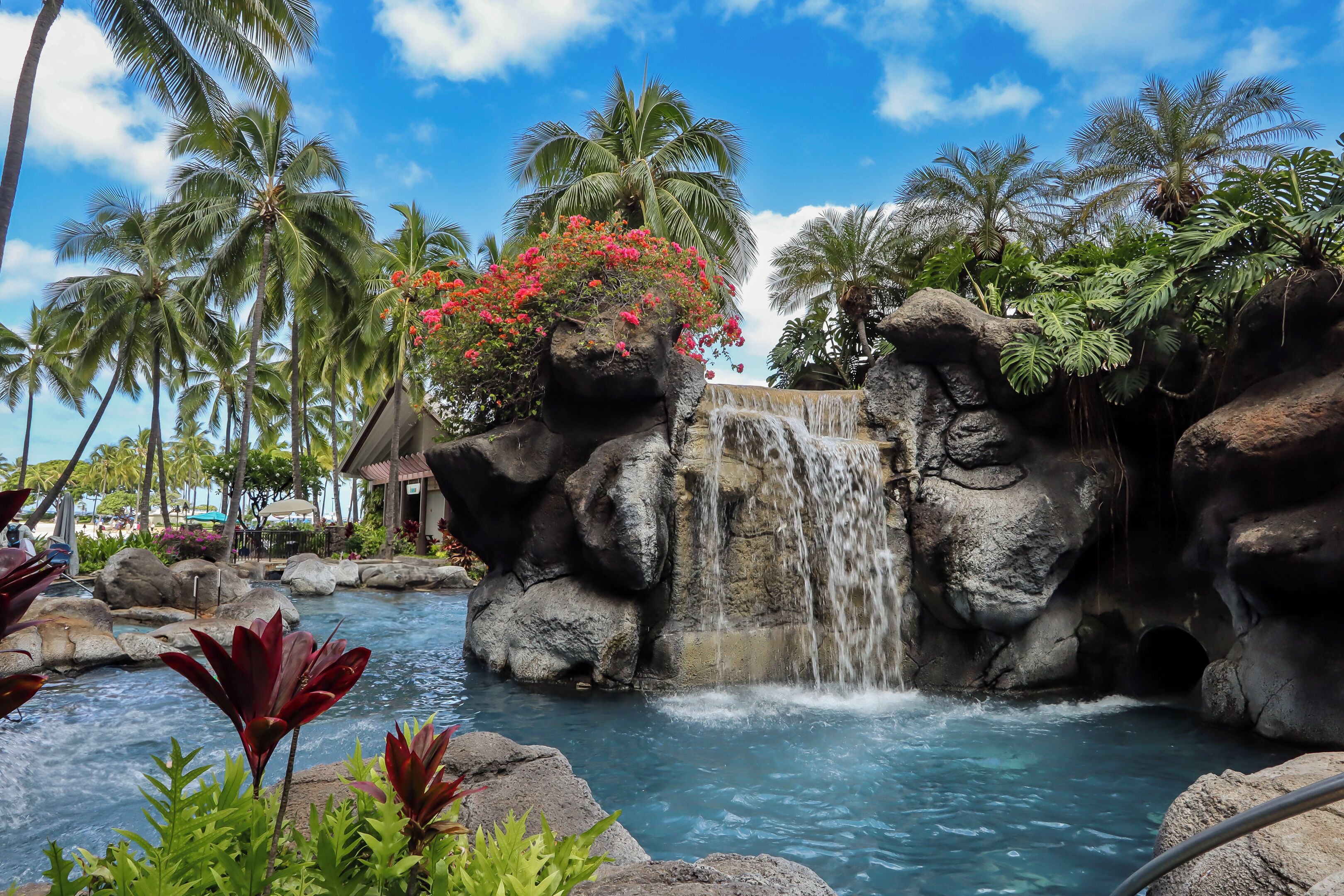 A tropical resort with a waterfall, palm trees, and a pool.