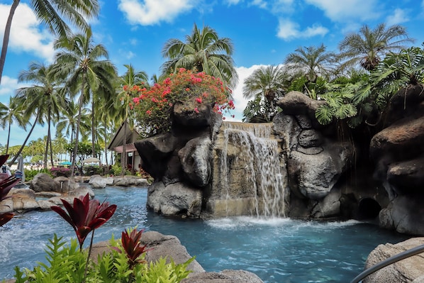 A tropical resort with a waterfall, palm trees, and a pool.