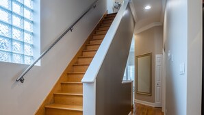 A staircase with wooden steps and a metal handrail, leading to a landing with a door and a window with a grid pattern. - NEW LUXURY PENTHOUSE CONDO (Chicago)
