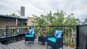 A wooden deck with two wicker chairs and a small table, surrounded by a metal railing. - NEW LUXURY PENTHOUSE CONDO (Chicago)
