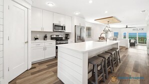 A modern kitchen with white cabinetry, a central island with stools, a microwave, stove, and refrigerator. - 🐚 Silver Beach Retreat | Beachfront | FREE VIP Package | Beach Chair Service (Destin)