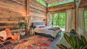 Une chambre avec un grand lit, un mur en bois, une fenêtre avec des rideaux, une chaise, une lampe sur pied et un tapis.