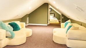 Een zolderkamer met twee roomkleurige banken, een vloerkleed en een trap naar een hoger gelegen verdieping.