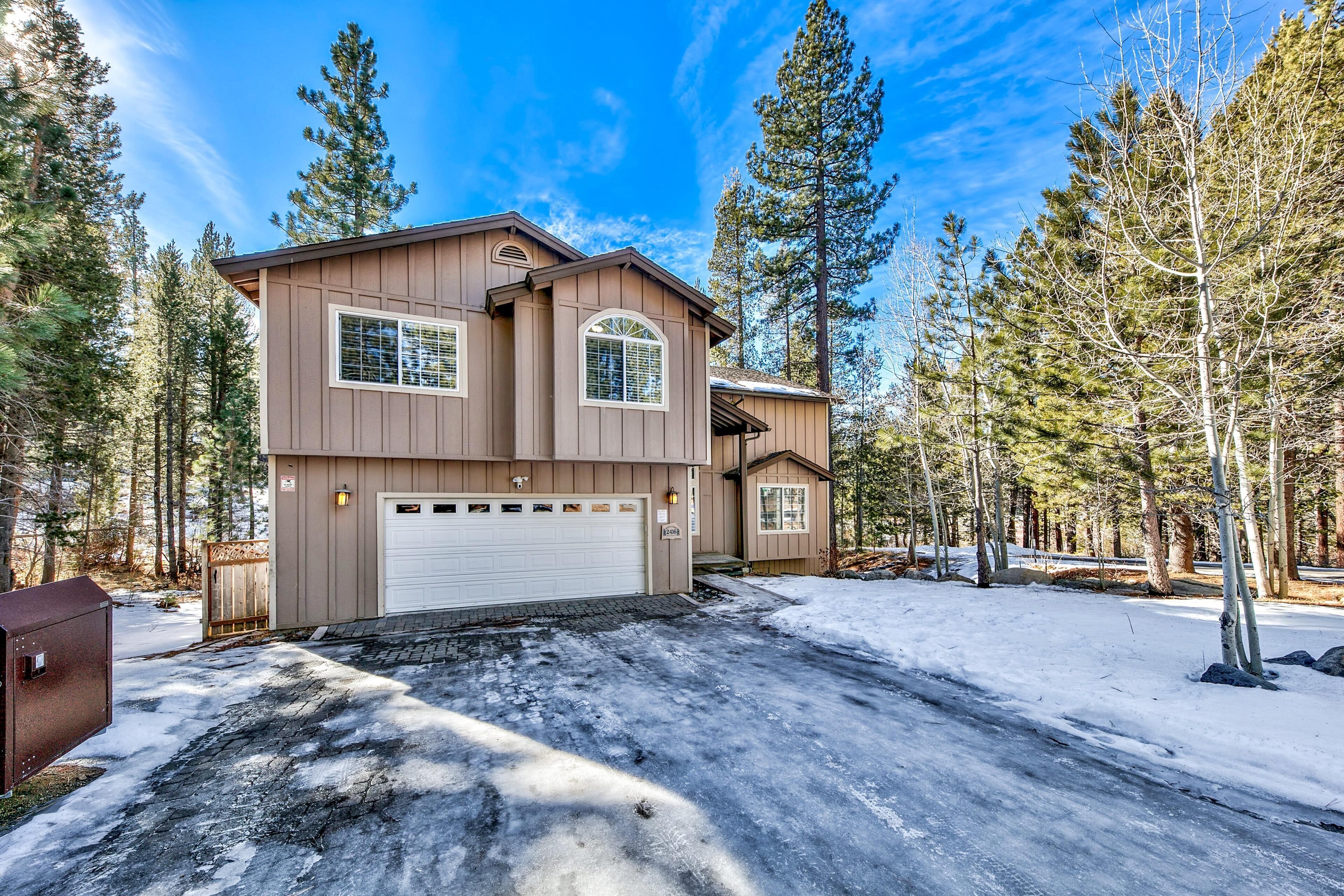 A two-story house with a garage, surrounded by a snowy landscape and tall pine trees.