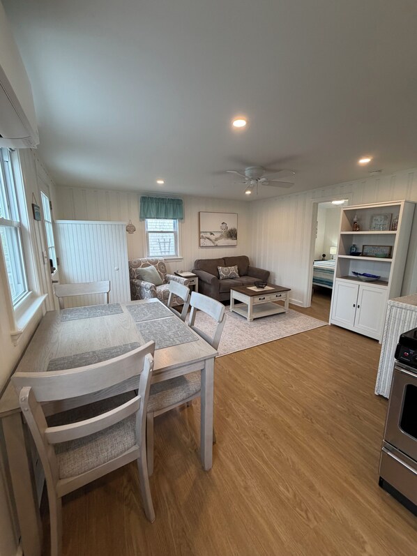 A dining area with a table and chairs, a sofa, a coffee table, and a kitchen area with cabinets and appliances.