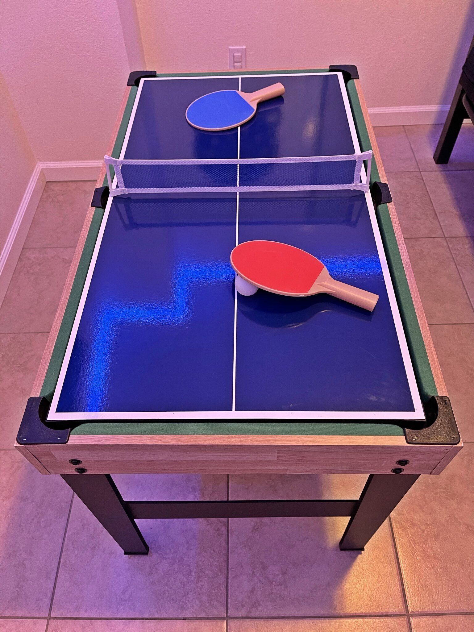 Ein Tischtennis-Tisch mit zwei Schlägern, einem blauen und einem roten, in einem Raum mit Fliesenboden.
