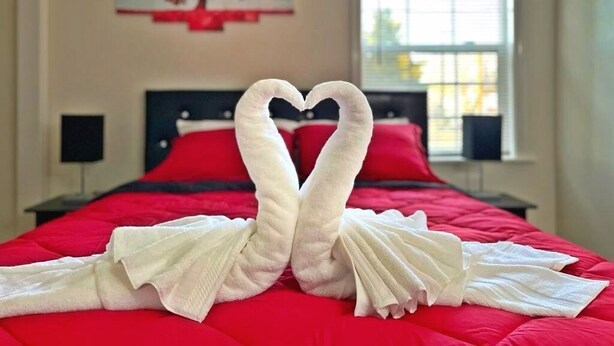 A hotel room with a red bedspread, a heart-shaped towel arrangement, and a painting on the wall. - ♥ Charming entire house in the heart of Lancaster ♥ (Lancaster)