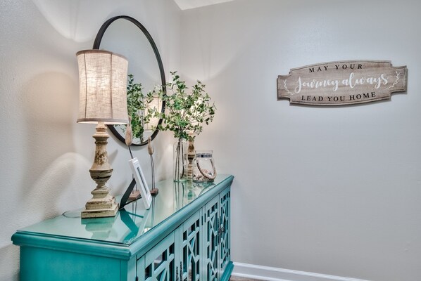 Ein turquoise Konsolentisch mit Lampe, einem Spiegel und Dekorationsobjekten, darunter ein Schild mit dem Schriftzug 'May your journey always lead you home.'