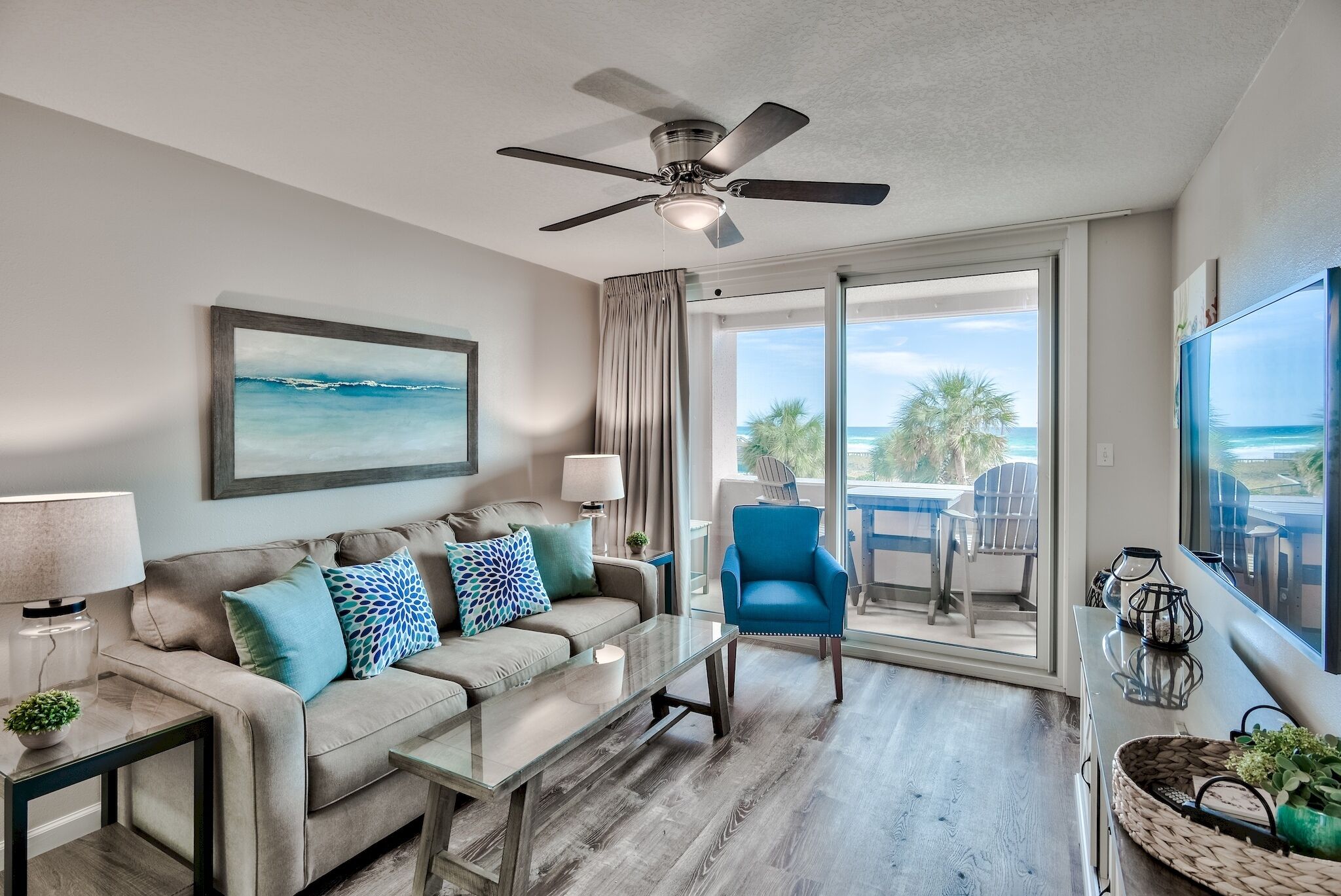 A modern living room with a ceiling fan, a sofa with patterned cushions, a coffee table, and a view of the ocean through large sliding glass doors.