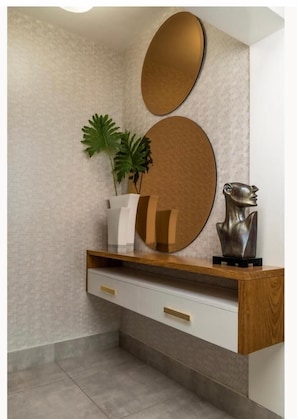 Contemporary space with a console table, round mirror, and metallic sculpture, featuring a neutral color palette and textured wall.