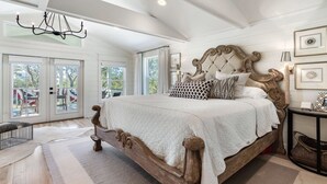 A spacious bedroom with a large bed, a chandelier, and a view of the outdoors through large windows. - 30A Home in Seacrest - PRIVATE POOL - Peak-A-Boo Ocean View 2 min Walk to Beach (Seacrest)