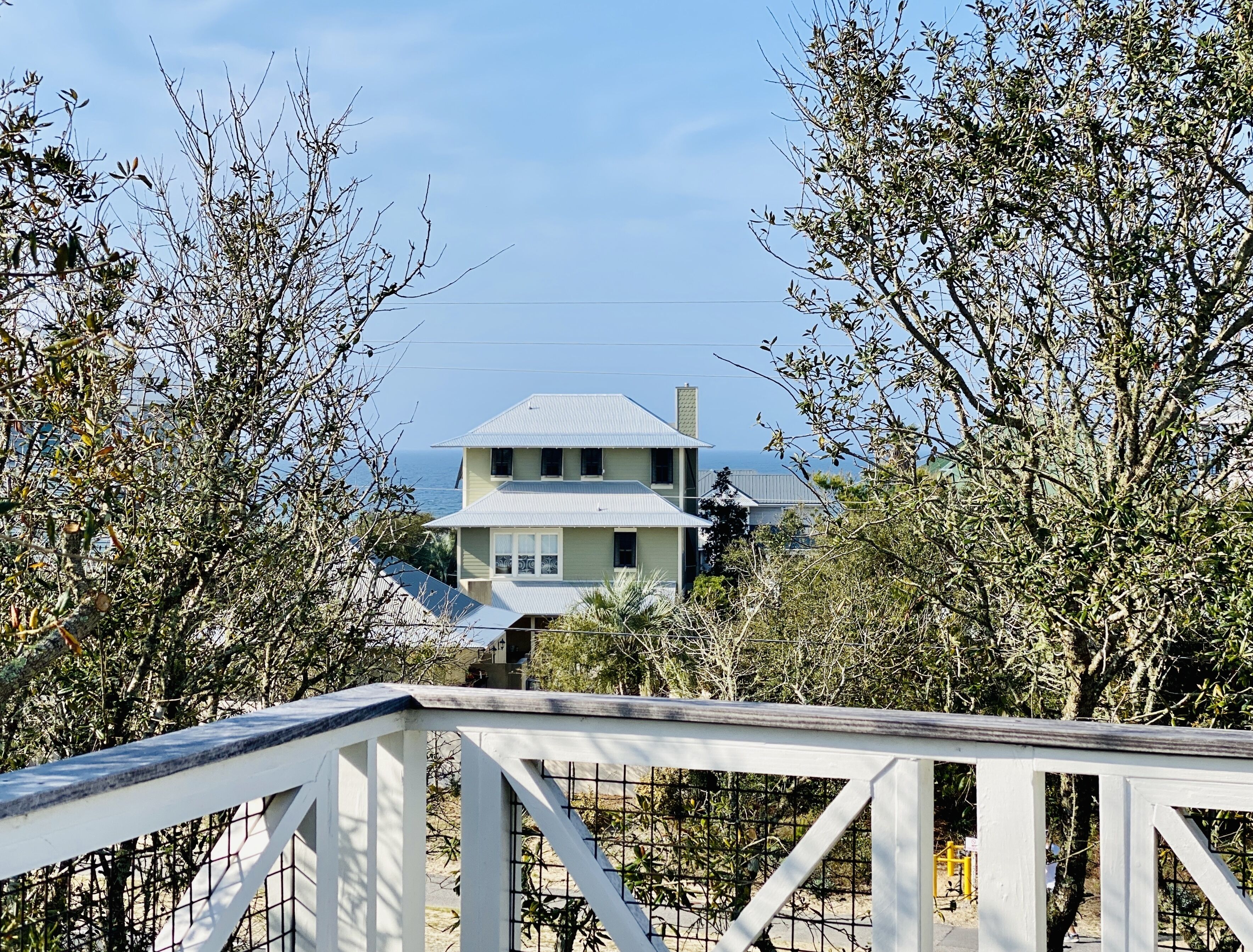 A two-story house with a gabled roof, surrounded by dense foliage and a clear view of the ocean.