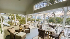 A covered porch with wicker furniture and a table, large windows, and a view of the street and trees. - 30A Home in Seacrest - PRIVATE POOL - Peak-A-Boo Ocean View 2 min Walk to Beach (Seacrest)