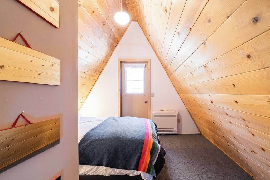 Ein kleiner, gemütlicher Raum mit Holzwänden und schrägen Decken, ein Bett mit farbenfroher Decke und ein Fenster, das für natürliches Licht sorgt.