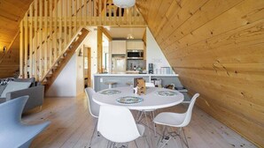 Un interno in legno con zona pranzo, un tavolo rotondo e sedie bianche, una cucina con elettrodomestici moderni e una scala in legno.