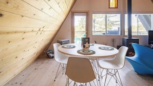 Una stanza accogliente con soffitto in legno spiovente, un tavolo rotondo con sedie, un divano blu e un camino.