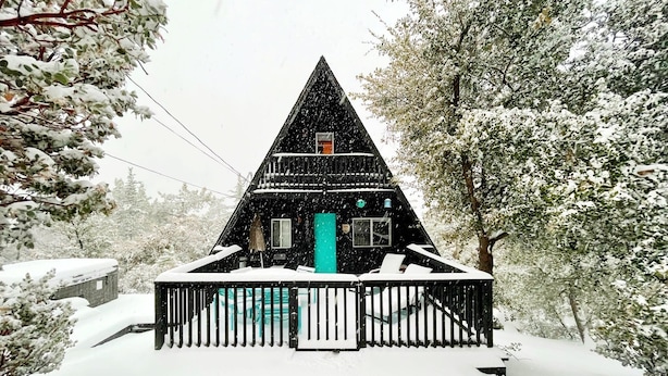 Una baita triangolare imbiancata dalla neve, con un portico e una porta verde.