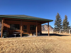 A log cabin with a covered porch, a barbecue grill, and a mountain view. - BISON HALLOW on the YELLOWSTONE RIVERFRONT (Gardiner)