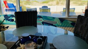 Vista desde una habitación con mobiliario de mimbre, una mesa de vidrio y vistas a la playa y las dunas.