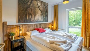 A bedroom with a large bed, a nightstand with a lamp, a painting of a forest, and a window with curtains. - Holiday Mountain Residence by Interhome (Swieradow Zdroj)