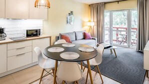 A modern kitchen with white cabinets, a microwave, and a coffee maker. There is a dining area with a round table and chairs, and a sofa with cushions. A lamp and a window with curtains are visible in the background. - Holiday Mountain Residence by Interhome (Swieradow Zdroj)