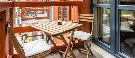 Una terraza de madera con una mesa y dos sillas, con vista a un edificio con balcones.