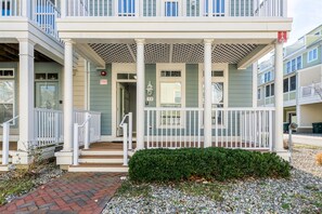 A multi-story building with a covered porch, white railings, and a brick pathway leading to the entrance. - Sunset Island 33 Sunset Island Drive (Ocean City)