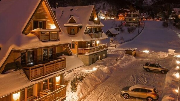 A snow-covered mountain village at night with traditional wooden houses, a ski slope, and a car parked in the snow. - Lipki Park Resort by Interhome (Zakopane)
