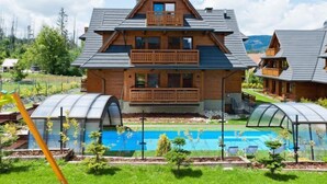 A two-story wooden cabin with a balcony, a swimming pool, and greenhouse structures. - Lipki Park Resort by Interhome (Zakopane)