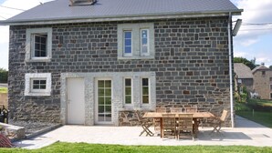 Une maison en pierre avec un patio, une table à manger et des chaises.