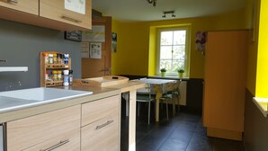Une cuisine avec des meubles de rangement en bois, un plan de travail, une fenêtre ornée de plantes et un coin repas avec des chaises.