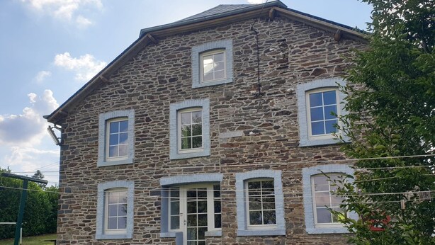 Un bâtiment en pierre doté de six fenêtres, d’une porte et d’un petit porche.