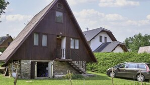 Une maison en bois avec des fondations en pierre, un petit porche et une voiture garée dans l’allée.