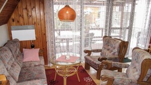 Un salon chaleureux avec un plafond en bois, un luminaire suspendu en osier, une table ronde en verre et des meubles à motifs floraux.
