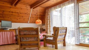 Une pièce chaleureuse avec des murs et un plafond en bois, un lit en bois, deux chaises en bois, une petite table, un téléviseur et une fenêtre avec des rideaux.