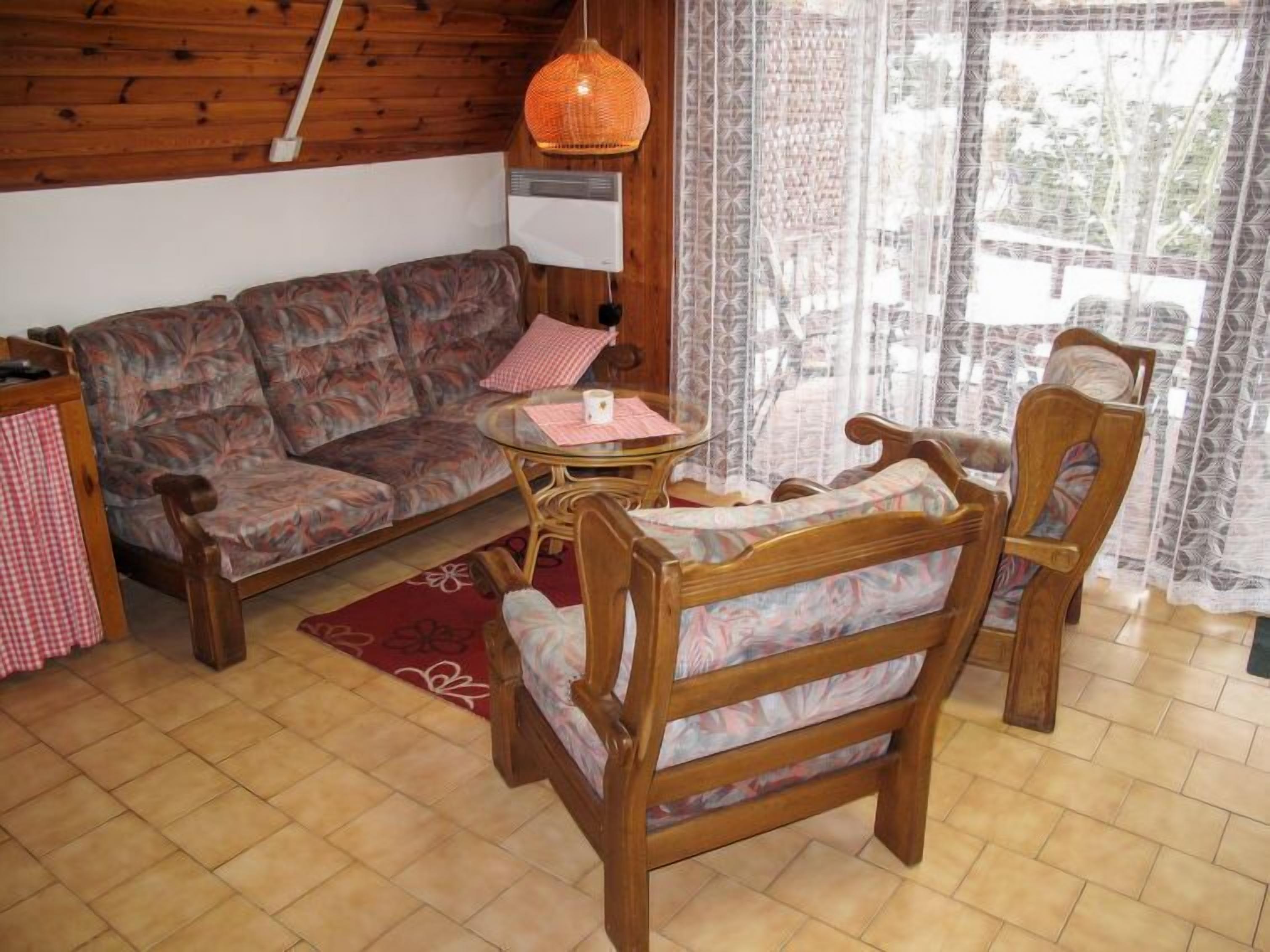 A cozy living room with a sofa, two wooden chairs, a small round table, and a hanging orange light fixture.