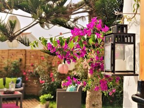 Enjoy a serene outdoor space surrounded by lush plants and vibrant flowers, featuring a cozy seating area with comfortable cushions.