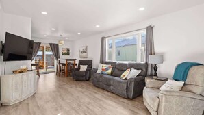 A modern living room with a grey sofa, a television, and a dining area with a table and chairs. - 63 Bar (Red Lodge)