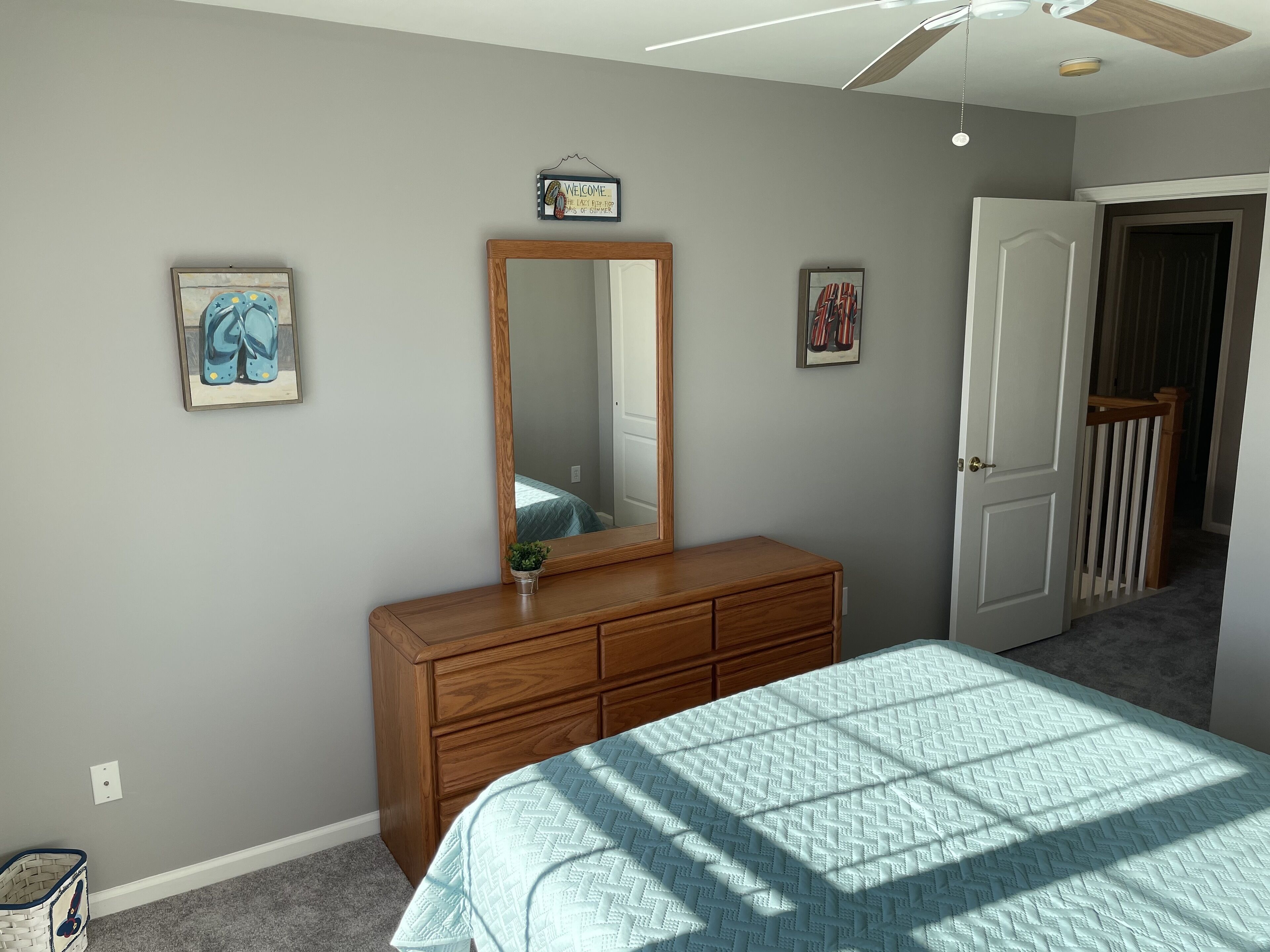 A bedroom with a bed, dresser, mirror, and a door leading to another room.